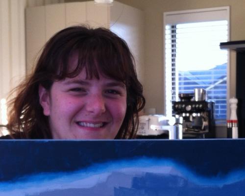 An image of Ashleigh smiling while she holds up on of her paintings.