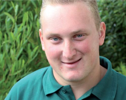 An image of Ricky smiling whilst in a garden.