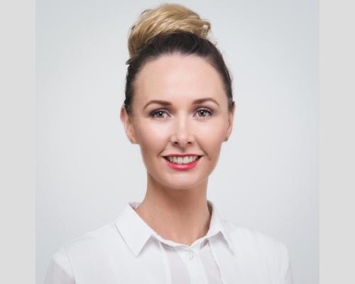 photograph. headshot taken on a white background, Carey-Ann Morrison with blonde hair pinned up in a loose bun.
Carey-Ann is wearing a white, collared shirt